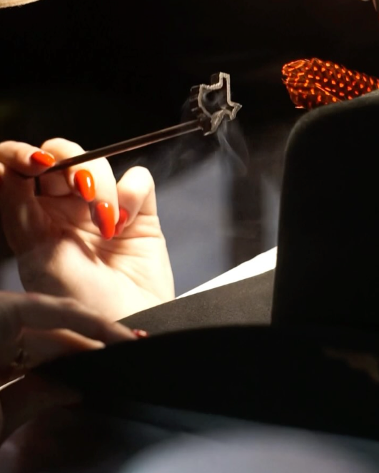A hand with bright orange nails holds metal tongs gripping a star-shaped object.