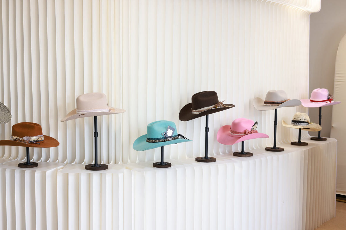 Row of styled cowboy hats on pedestal stands against a fluted white display counter at Basila Frocks
