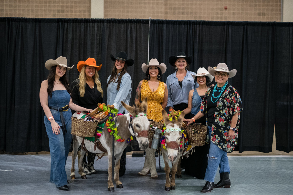 Group of women in cowboy hats with donkeys in a courtyard. Wild pony hat bar.