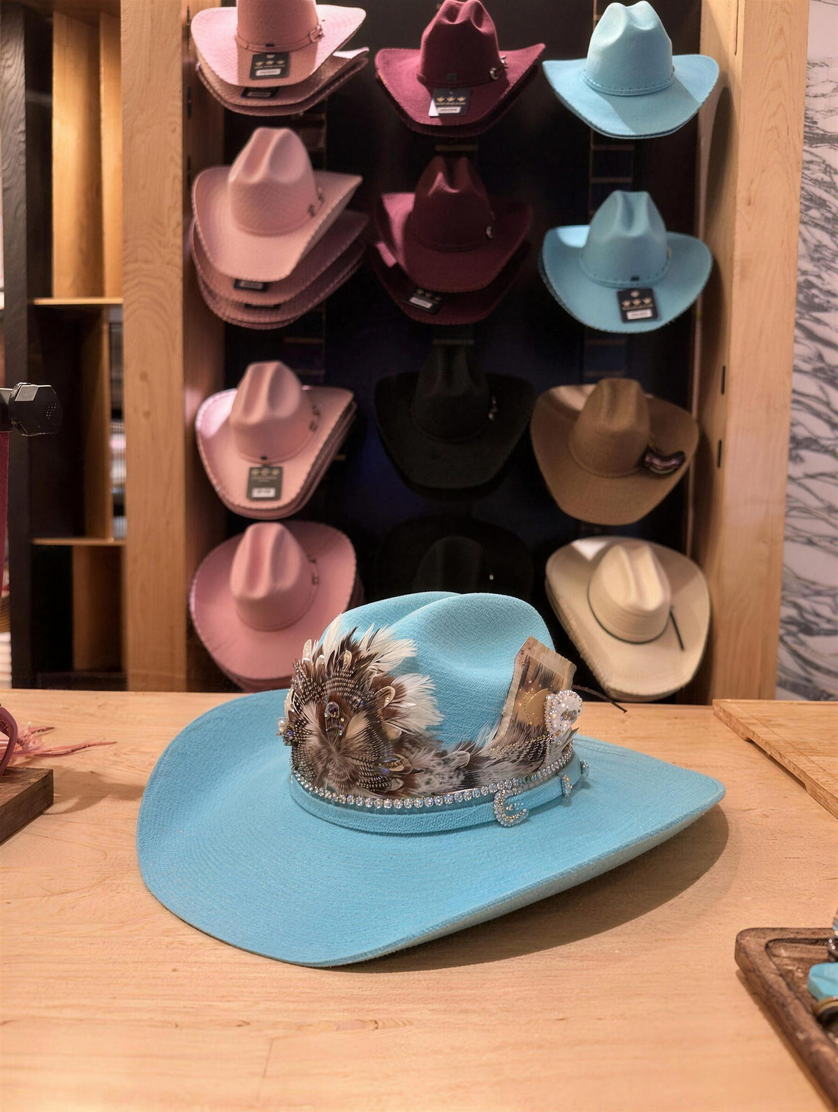 Turquoise custom cowboy hat with feathers in front of a wall of felt hats