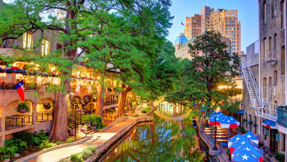 The San Antonio River Walk at dusk, lined with cypress trees and patio umbrellas