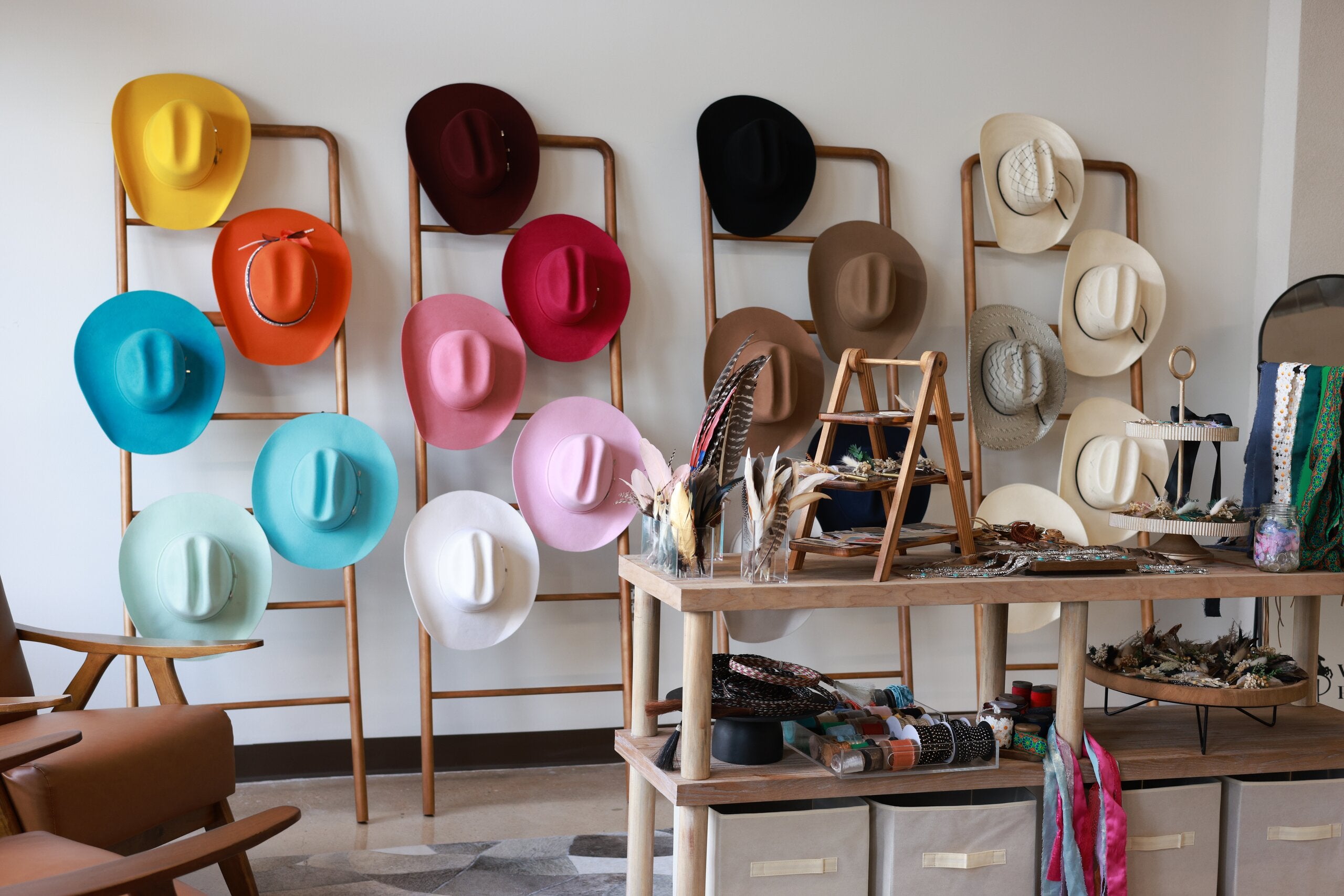 Wall of custom felt cowboy hats in every color on wood ladder racks beside a styling table of hat bands at Wild Pony inside Basila Frocks