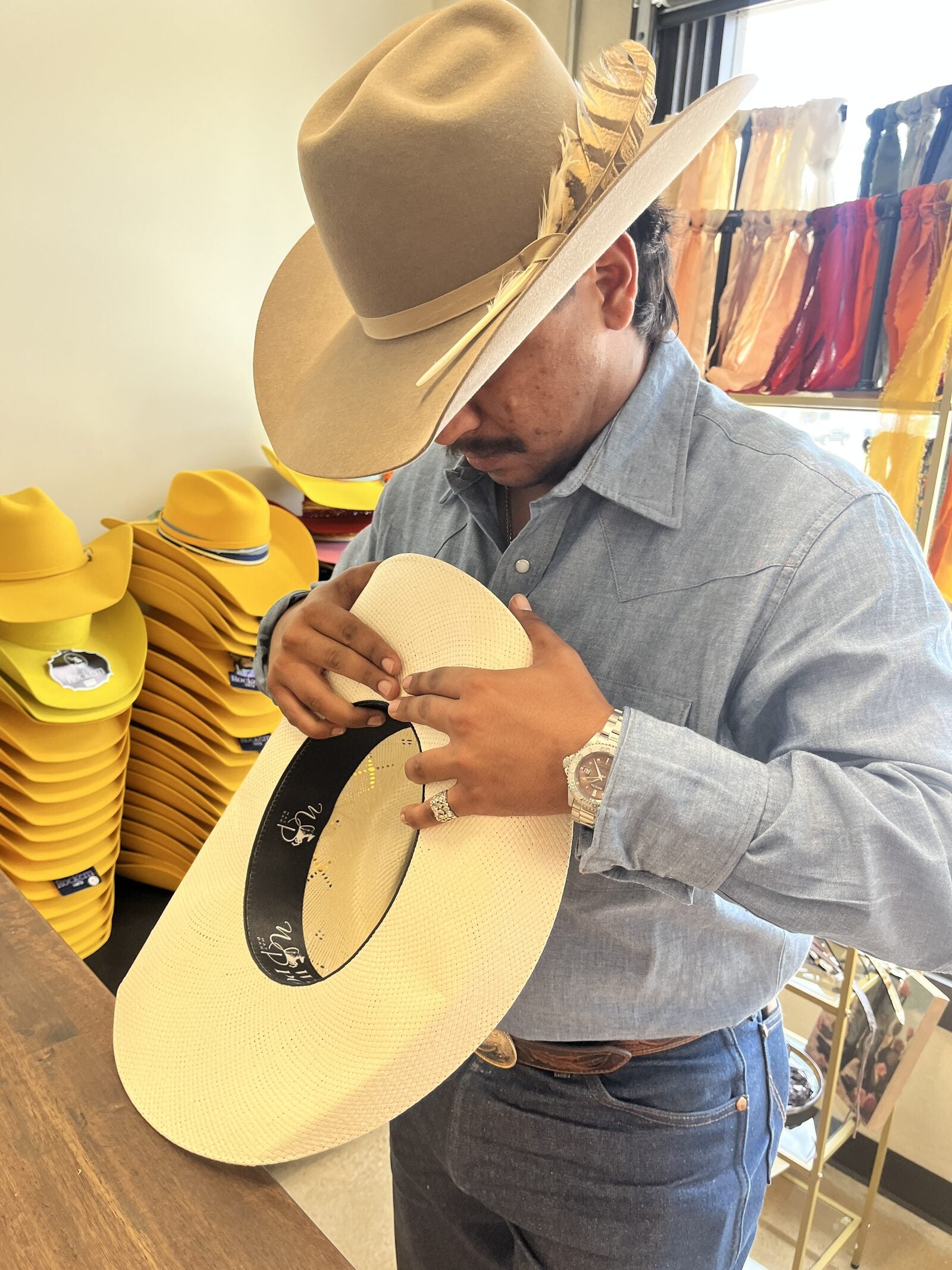 Wild Pony hat maker in a tan felt hat shaping and banding a straw cowboy hat at Basila Frocks in San Antonio