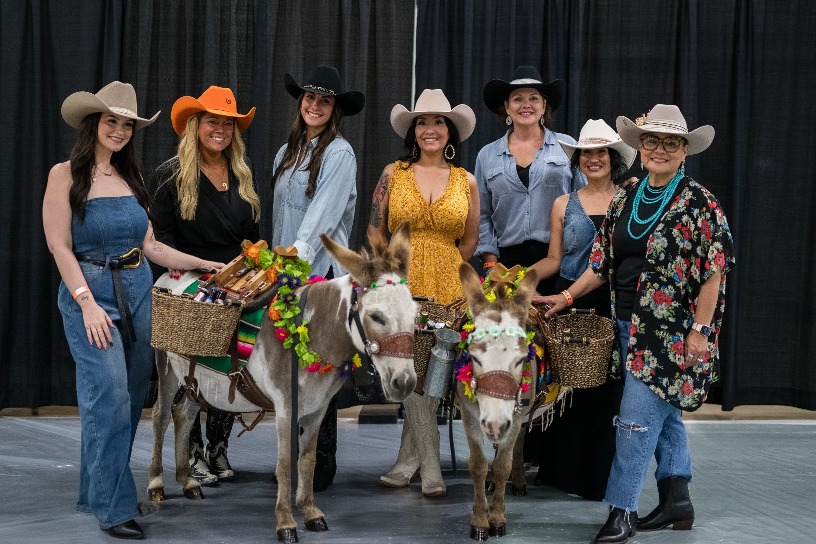 Group of women in cowboy hats with donkeys in a courtyard. Wild pony hat bar.